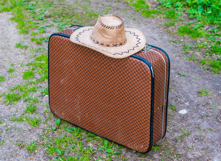 Old suitcase with a hat on a country road.