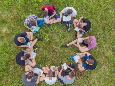 Teamwork concept. A group of high school students sit on the grass in a circle and scatter in...