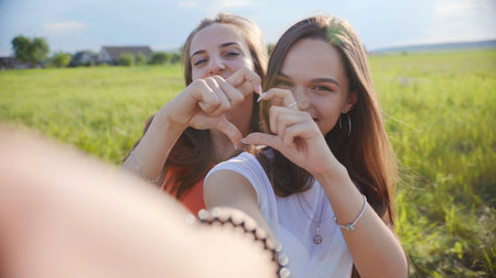 Girlfriends take selfies and heart shapes from their hands.