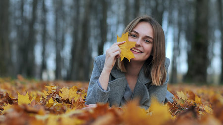 Beautiful happy young girl with a smile holds an autumn yellow leaf near the face.