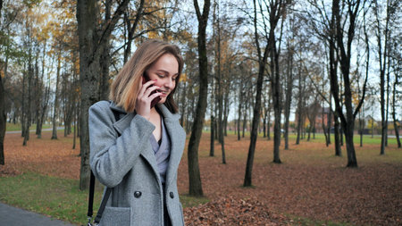 A young girl walks through the autumn park and dials a number on the phone.