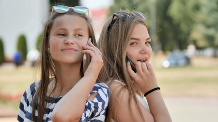 Two young girls talking on the phone on a summer day.