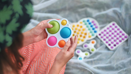 Teen girl plays with anti-stress multicolored toys popit and simple dimple in the park on a summer...