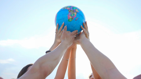 The concept of saving the world. A group of friends raise a world globe in their hands.の写真素材