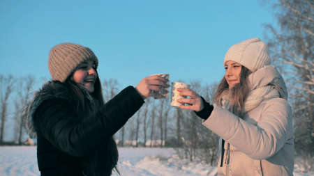Two friends drink hot tea in winter and clink glasses hugging.の写真素材