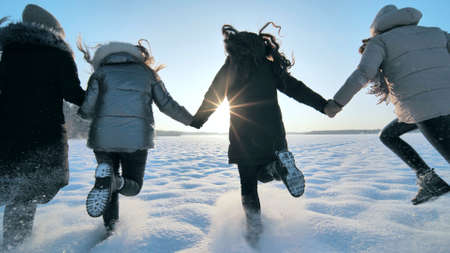 Cheerful girls run hand in hand across a snowy field.の写真素材