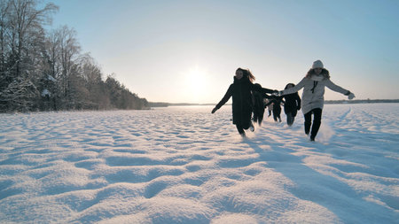 Cheerful girls run hand in hand across a snowy field.の写真素材