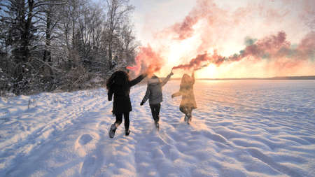 Girls friends run across the winter field with colored smoke.の写真素材