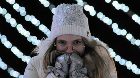 The girl freezes in the evening in the city in winter against the background of gerlands.の写真素材