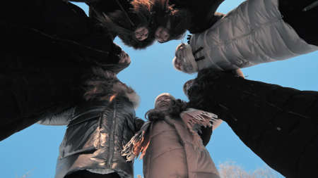 Girls in a circle hug each other on a winter day against a blue sky.の写真素材