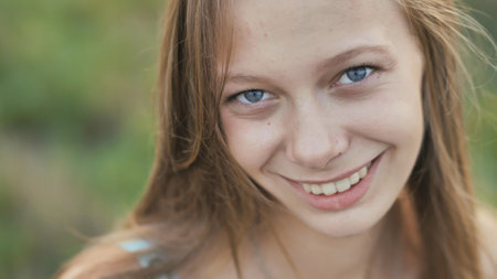 Portrait of a young smiling sixteen-year-old girl with a daisy flower in her hands. Brown-haired girl with long hair.. Face close-up.の写真素材