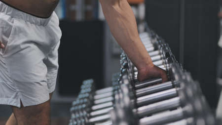 Arab man athlete is grabbing a dumbbell from a big selection in a fitness center.の写真素材