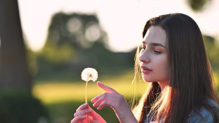A young girl gently looks at the dandelion flower.