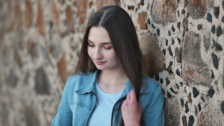 Portrait of a long-haired girl in a denim jacket against a stone wall.