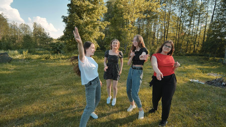 Joyful girls are dancing on a picnic near the forest.