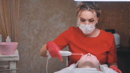 A beautician makes a darsonvalization of the face of a young girl with problem skin.の写真素材