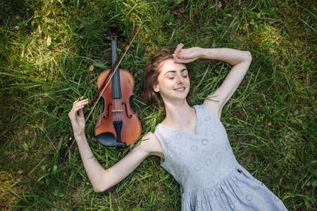 The girl lies with a violin on the grass in a city park.の写真素材