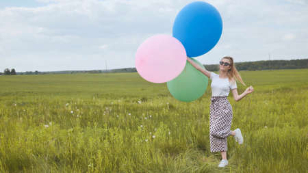 Happy girl with big multicolored balloons posing on the field.の写真素材