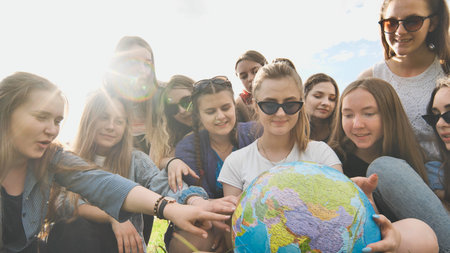 A group of cheerful girls is exploring the globe of the world in the meadow.