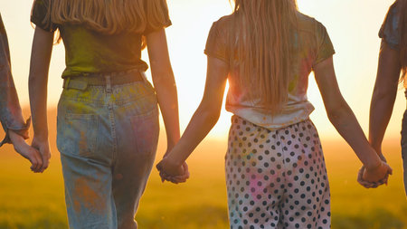 Eleven cheerful girls run to the meeting across the field in the summer, holding hands.