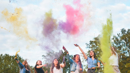 Cheerful girls toss up multi-colored powder at a beautiful sunset.
