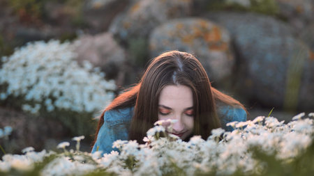 Long-haired girl sniffs white flowers and smiles.