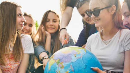 A group of cheerful girls is exploring the globe of the world in the meadow.の写真素材