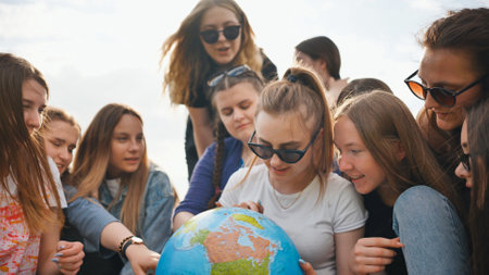 A group of cheerful girls is exploring the globe of the world in the meadow.の写真素材