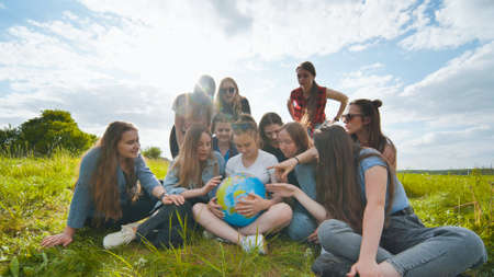 A group of female students are sitting in a meadow and studying the globe of the world.の写真素材