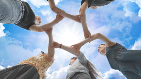 Friends join their hands by the wrist and make a circle against the backdrop of a fabulous sky. Strong friendship concept.の写真素材