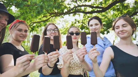 Girlfriends hold chocolate ice cream on a stick in a row.の写真素材