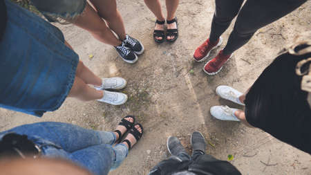Legs and sneakers of teenage boys and girls standing in half circle on the sand.の写真素材