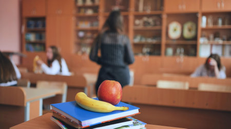 An apple and a banana lie on the books in an empty classroom between lessons.の写真素材