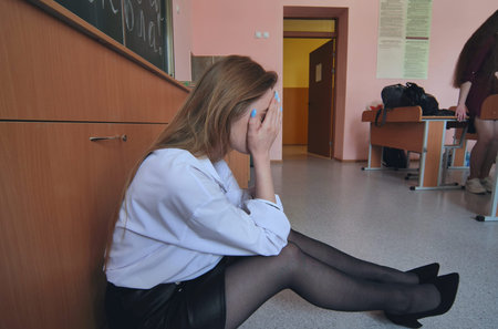 Pupils run to calm down their friend who is crying on the floor in the classroom.