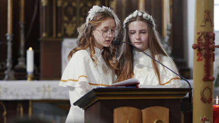 Lyadsk, Belarus - May 2, 2021: Girls read the gospel at the first communion of children in a Catholic church.のeditorial素材