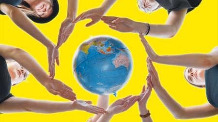 Schoolgirls hug the earth globe with their hands, making a circle out of them on a yellow background.の写真素材