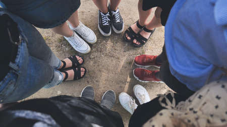 Legs and sneakers of teenage boys and girls standing in half circle on the sand.の写真素材
