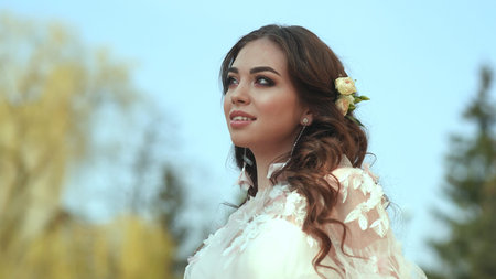 The bride in a white dress shows beautiful makeup on her face in the street.