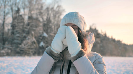 A young girl in mittens is drinking hot coffee in winter.