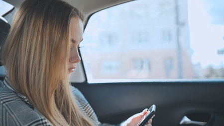 A young girl rides in the backseat of a car and watches her smartphone.