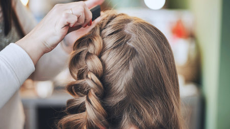 The girl makeup artist makes a braid for the model.