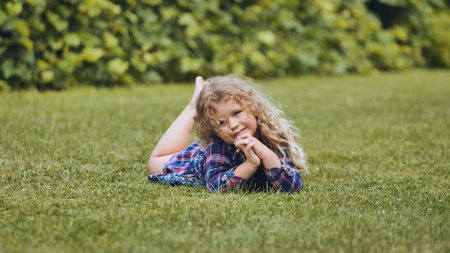 A little curly-haired girl lies on the grass in the garden.の写真素材