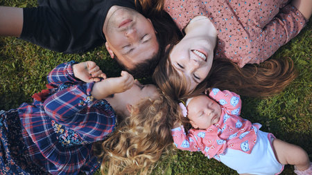 A young family lies on the grass in the garden in the summer.