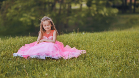A little girl is sitting in a pink dress in the park.の写真素材