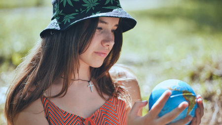 A teenage girl in a panama hat is looking at a globe of the earth.の写真素材