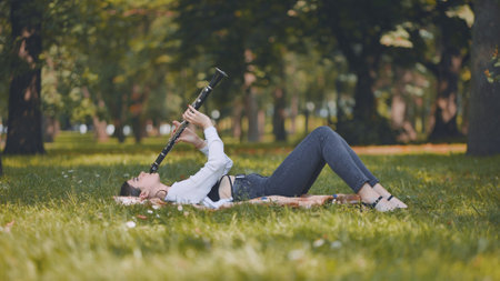 A girl plays the clarinet while lying on the grass in the park.の写真素材