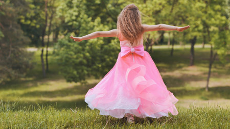 A girl in a pink princess dress is spinning in the park.の写真素材