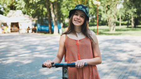 Portrait of a girl on an electric scooter posing in a park in the summer.の写真素材