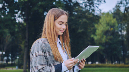 A young girl walks with a tablet in the park.の写真素材