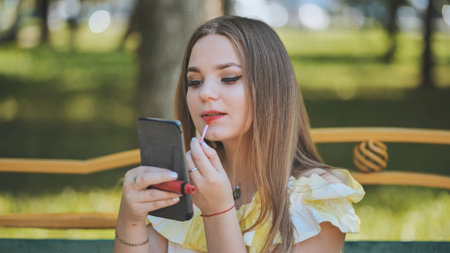 A girl paints her lips in the park in the summer.の写真素材